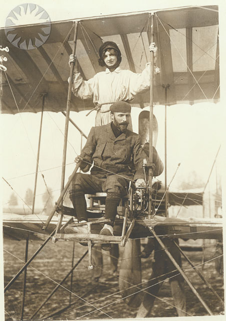 Close-up view of Henri Farman and standing behind is Madame Dacty secured by a rope around her waist, photographed prior to take off, at Etampes, France, September 21, 1913.